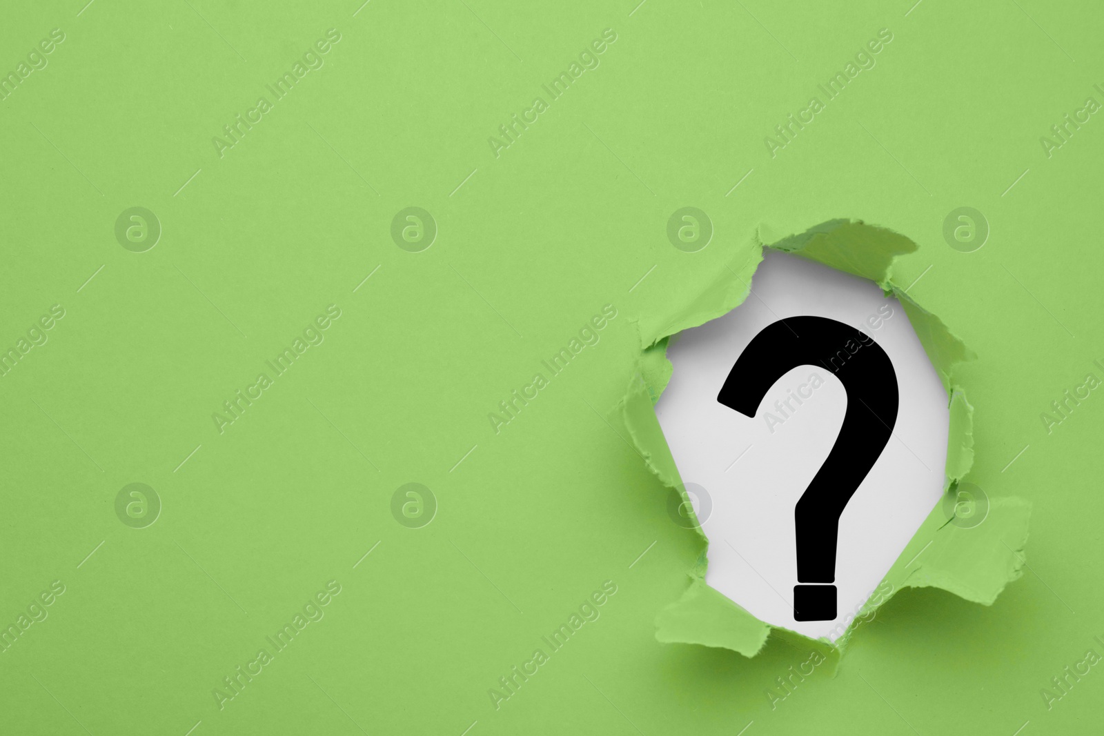 Photo of Question mark on white background, view through hole in light green paper, space for text