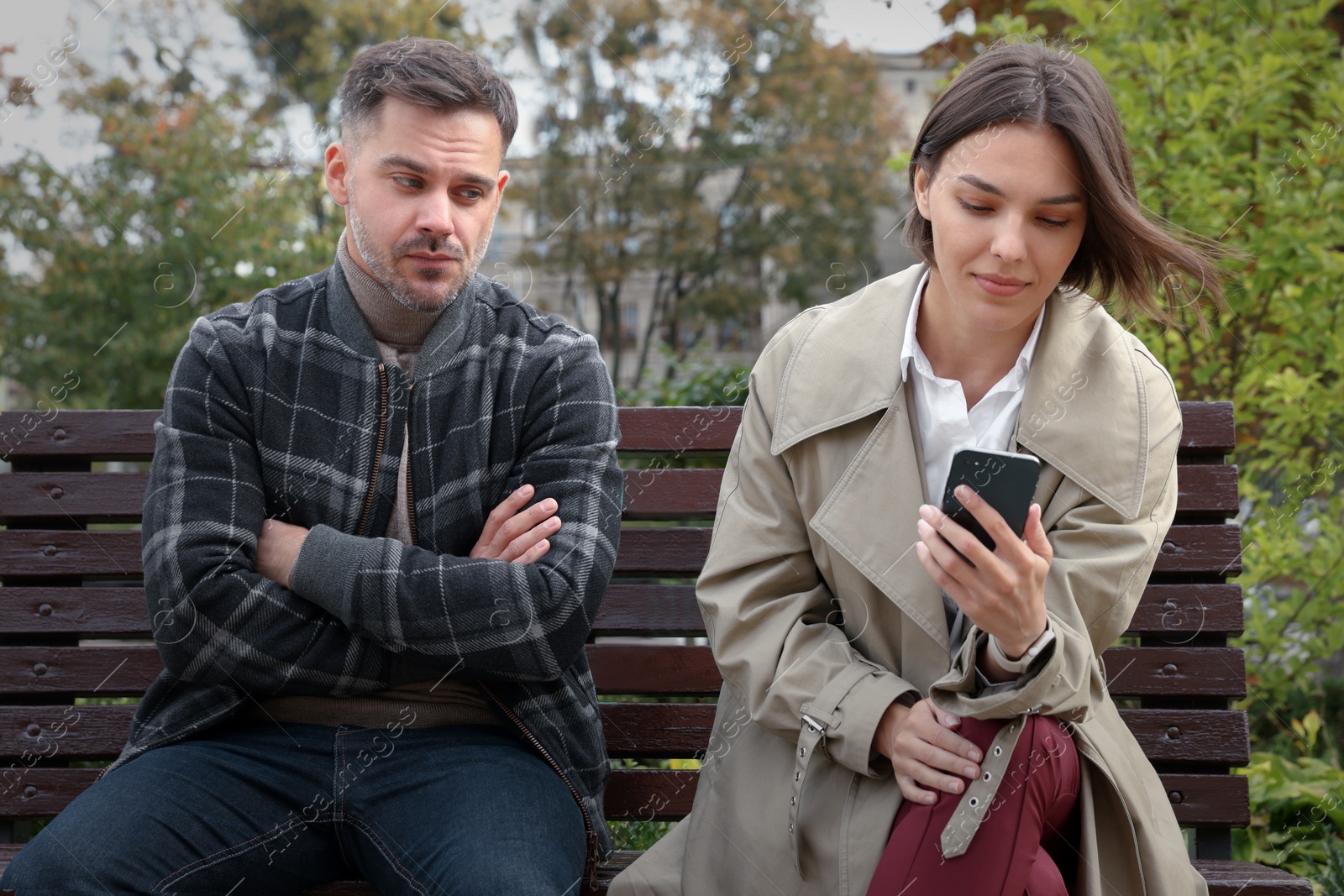 Photo of Distrustful man peering into girlfriend's smartphone outdoors. Relationship problems