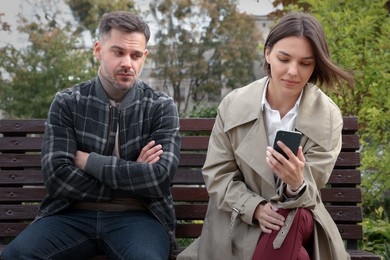 Photo of Distrustful man peering into girlfriend's smartphone outdoors. Relationship problems