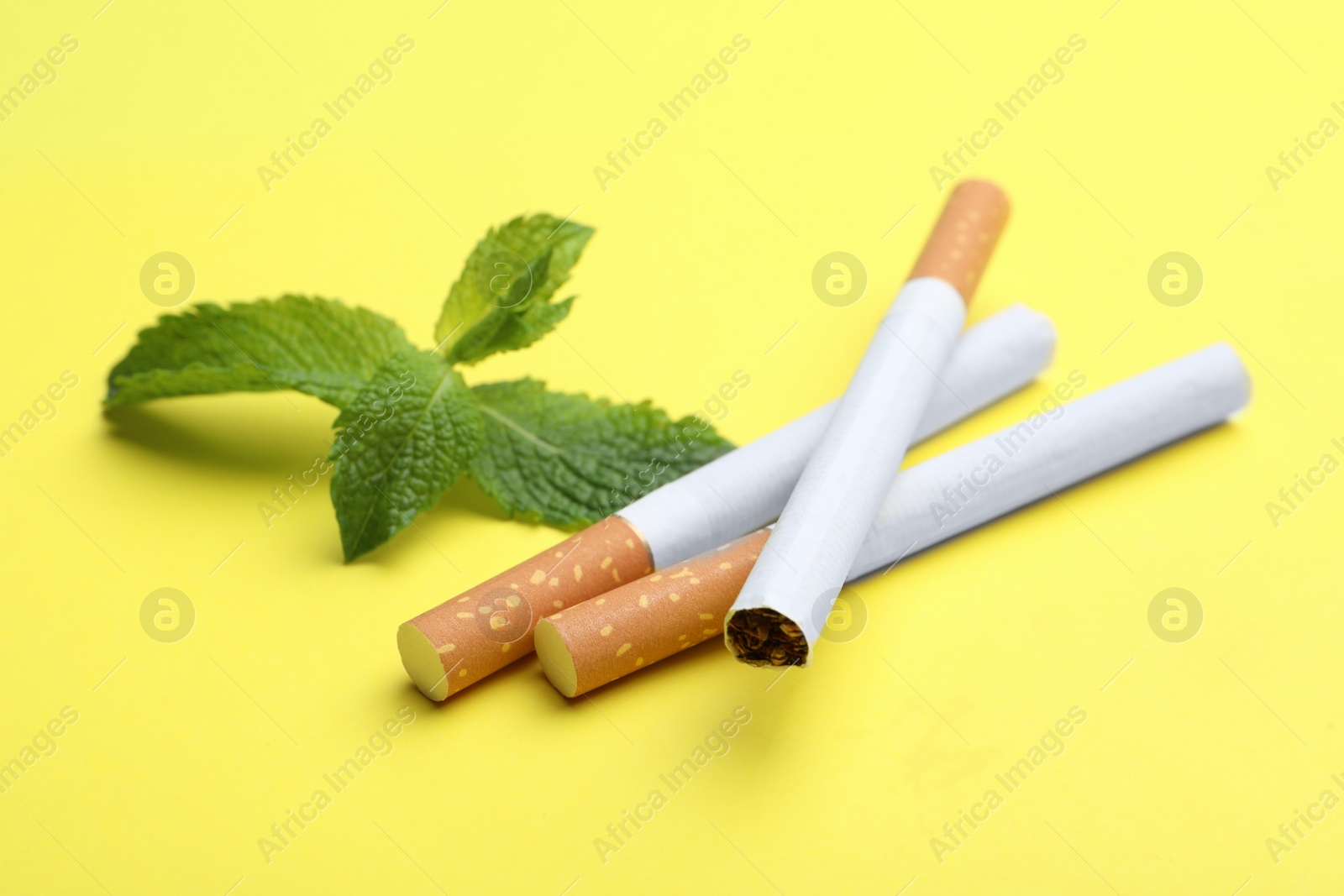 Photo of Menthol cigarettes and mint on yellow background