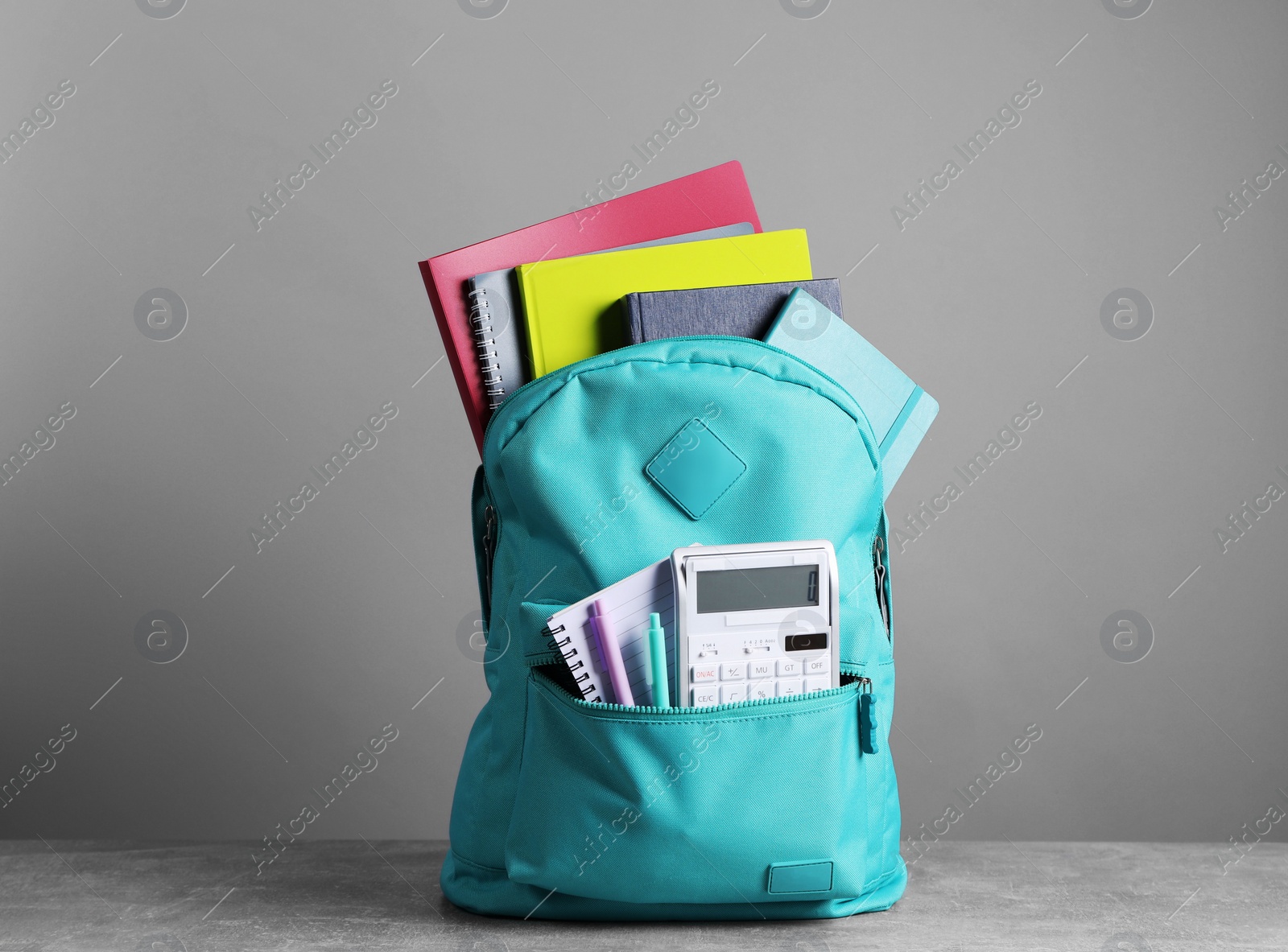 Photo of Turquoise backpack and different school stationery on table against grey background