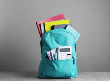 Photo of Turquoise backpack and different school stationery on table against grey background