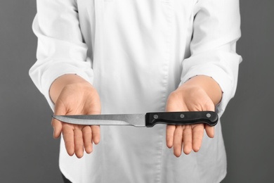 Woman holding carving knife on grey background, closeup