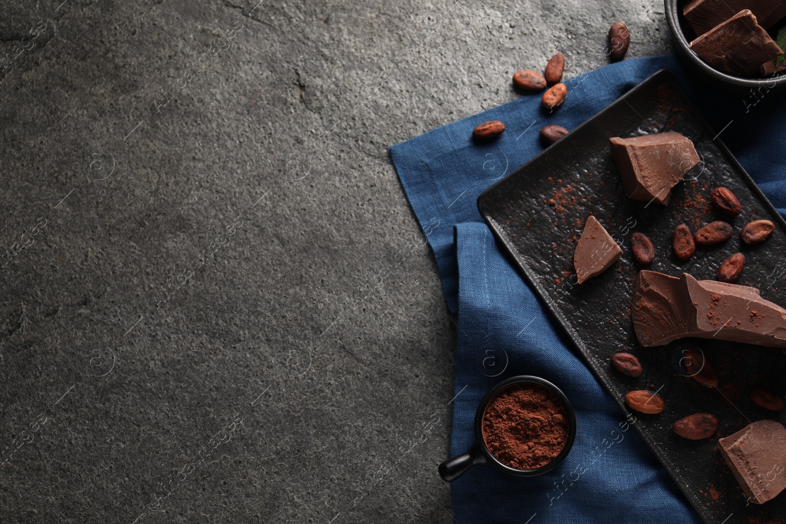 Photo of Pieces of tasty milk chocolate, cocoa beans and powder on grey textured table, top view. Space for text