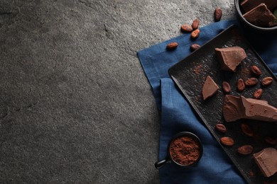 Photo of Pieces of tasty milk chocolate, cocoa beans and powder on grey textured table, top view. Space for text