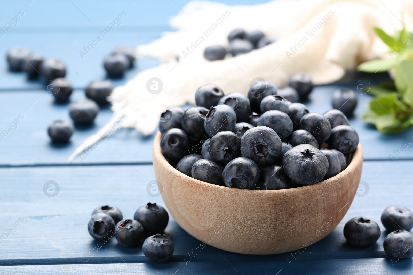 Photo of Tasty fresh blueberries and green leaves on blue wooden table, closeup