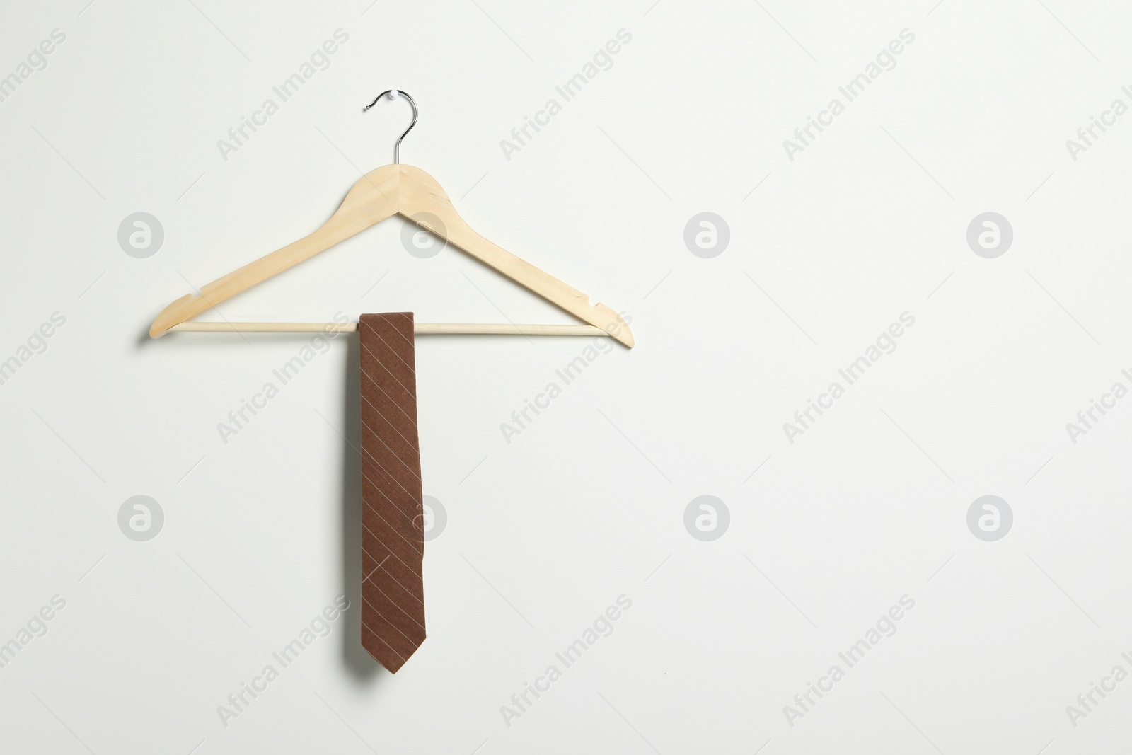 Photo of Hanger with striped necktie on white wall. Space for text