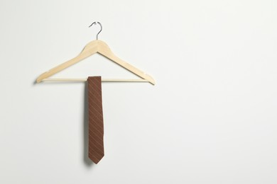 Photo of Hanger with striped necktie on white wall. Space for text