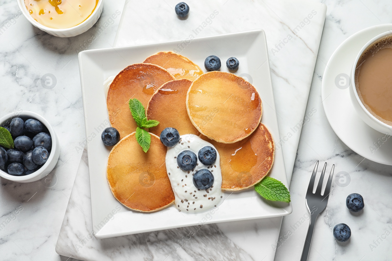 Photo of Plate of tasty pancakes with blueberries, sauce and mint on white marble table, flat lay