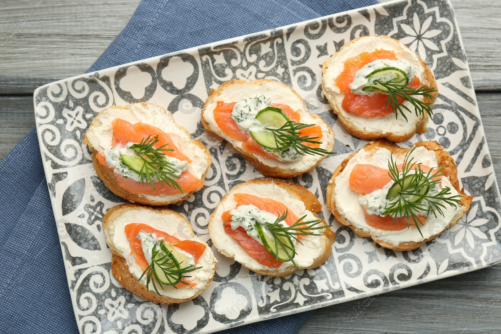 Photo of Tasty canapes with salmon, cucumber, cream cheese and dill on wooden table, top view