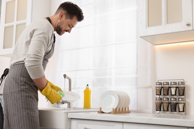 Photo of Man washing plate above sink in kitchen