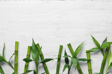 Photo of Green bamboo stems on white wooden background, top view. Space for text