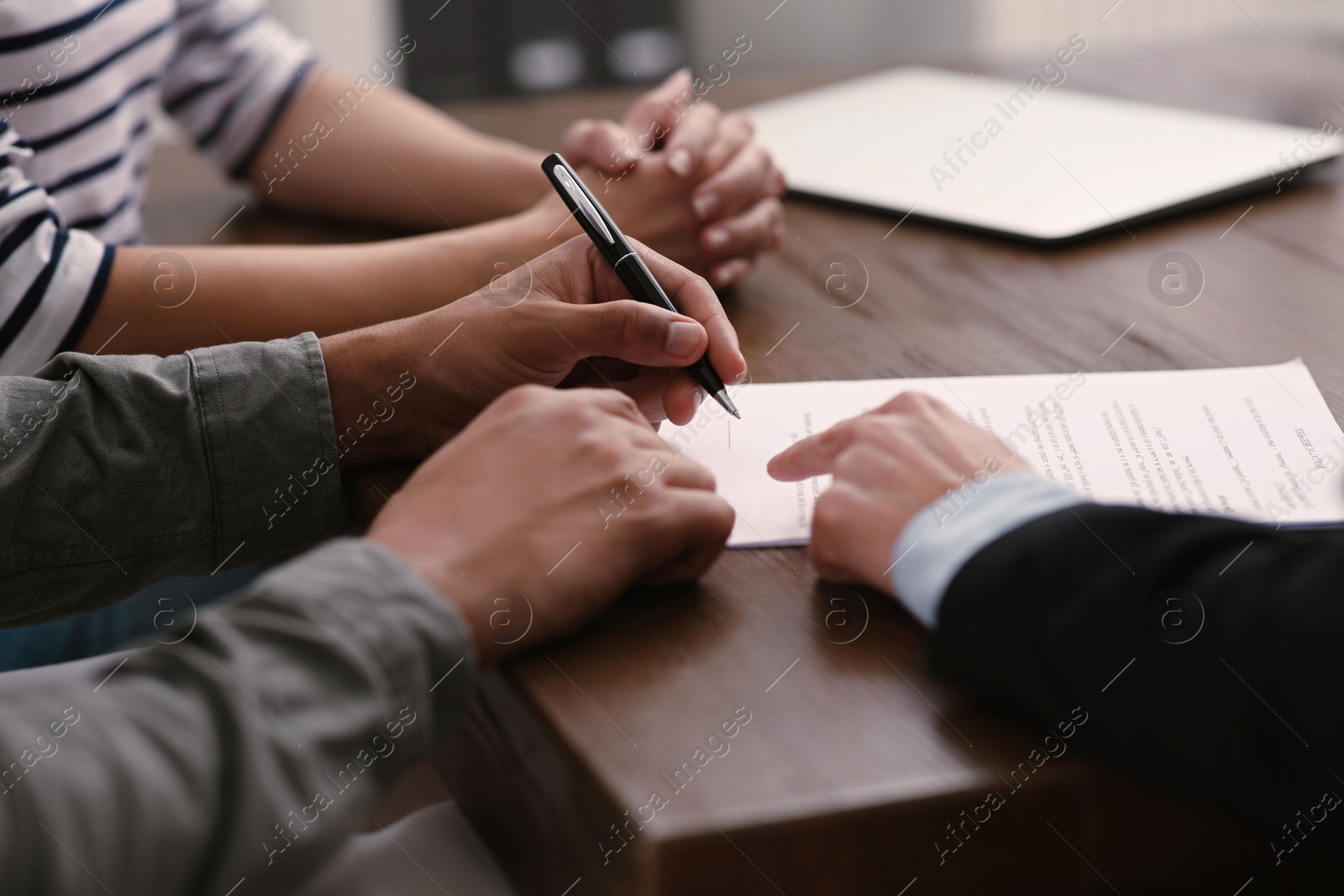 Photo of Notary helping couple with paperwork at wooden table, closeup