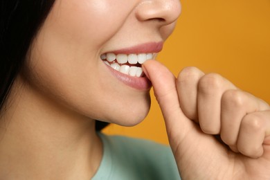 Photo of Young woman biting her nails on yellow background, closeup