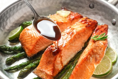 Pouring sauce onto tasty cooked salmon in frying pan, closeup