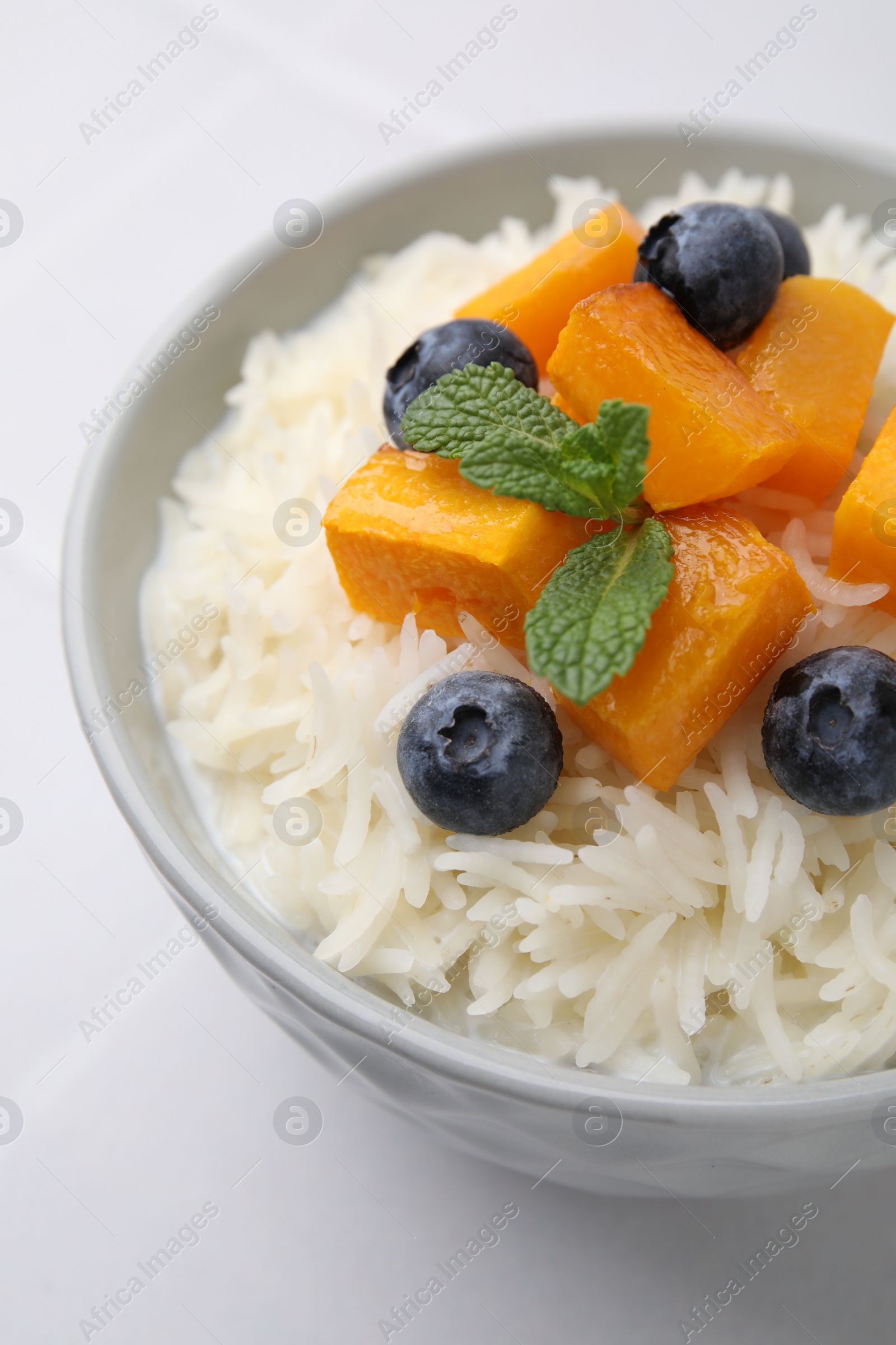 Photo of Bowl of delicious rice porridge with blueberries and pumpkin on white table, closeup