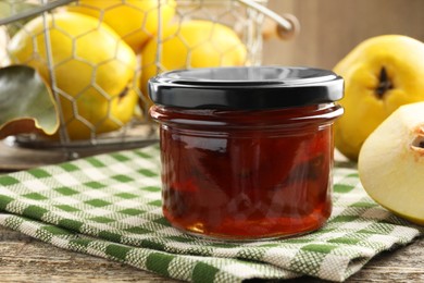 Photo of Tasty homemade quince jam in jar and fruits on wooden table, closeup