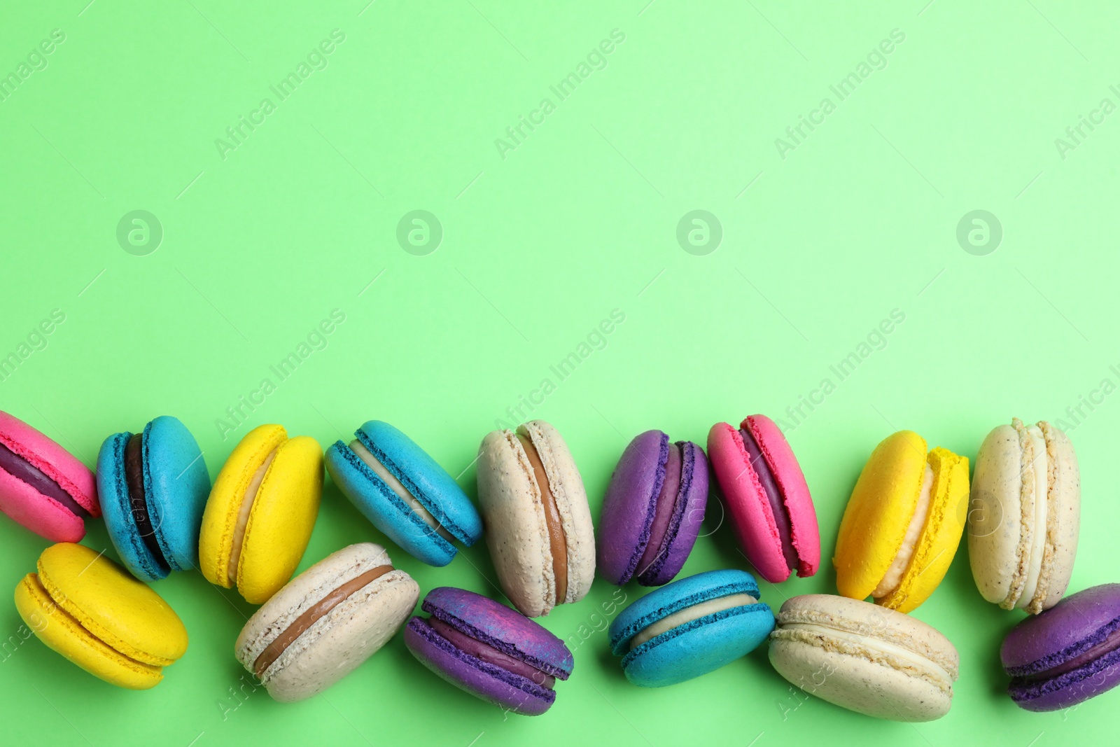 Photo of Delicious colorful macarons on green background, flat lay. Space for text