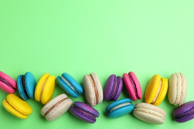 Delicious colorful macarons on green background, flat lay. Space for text