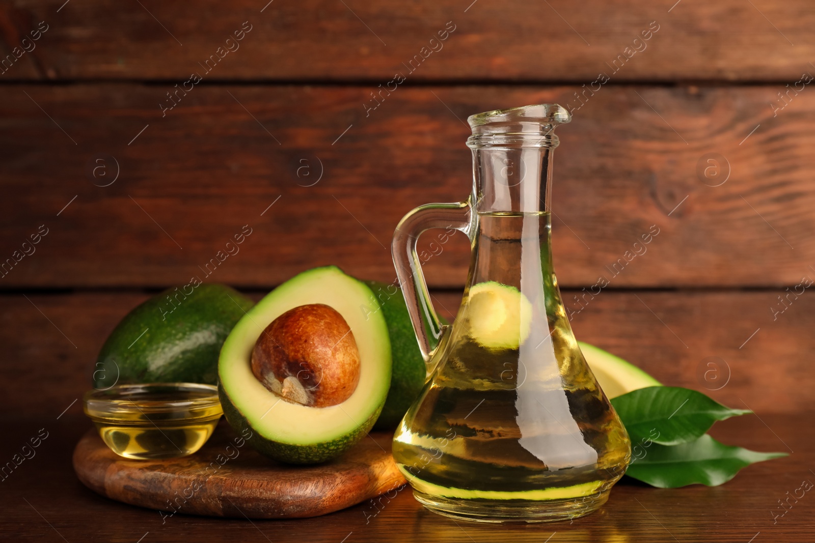 Photo of Glass jug of cooking oil and fresh avocados on wooden table