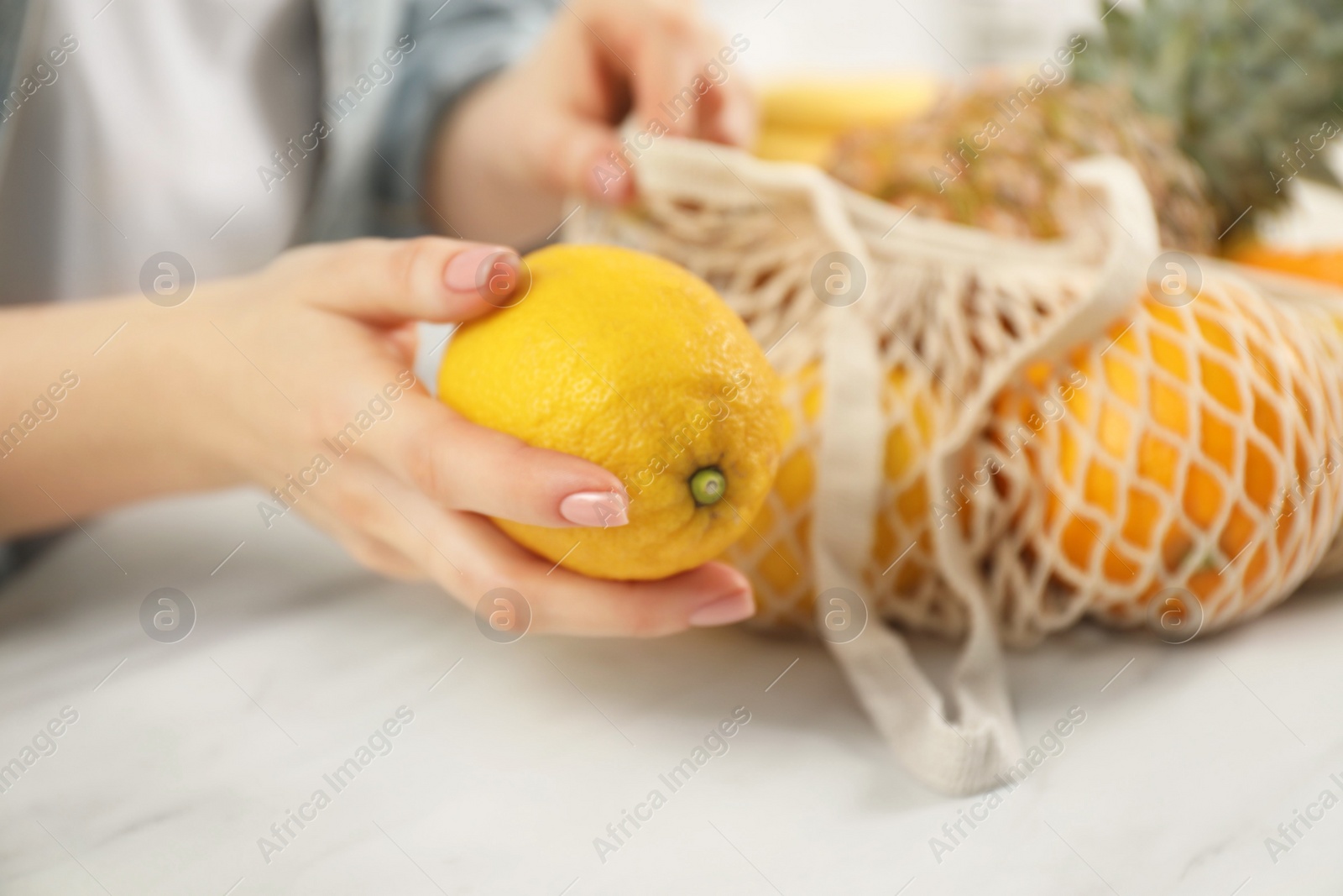 Photo of Woman with string bag of fresh fruits and lemon at light table, closeup