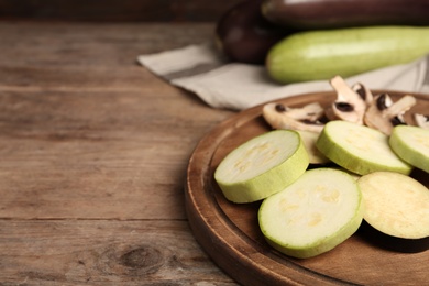 Photo of Slices of fresh zucchini and mushrooms on wooden table, closeup. Space for text