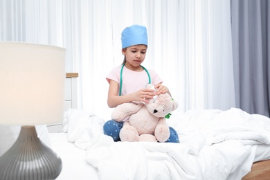 Photo of Cute child playing doctor with stuffed toy on bed in hospital ward