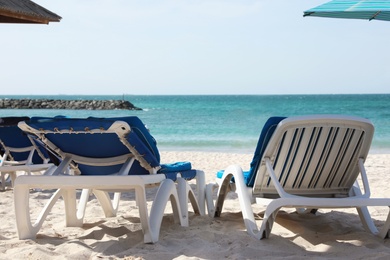 Photo of Comfortable sunbeds on sandy beach at tropical resort