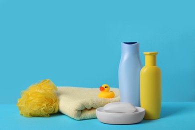 Photo of Baby cosmetic products, bath duck, sponge and towel on light blue background. Space for text