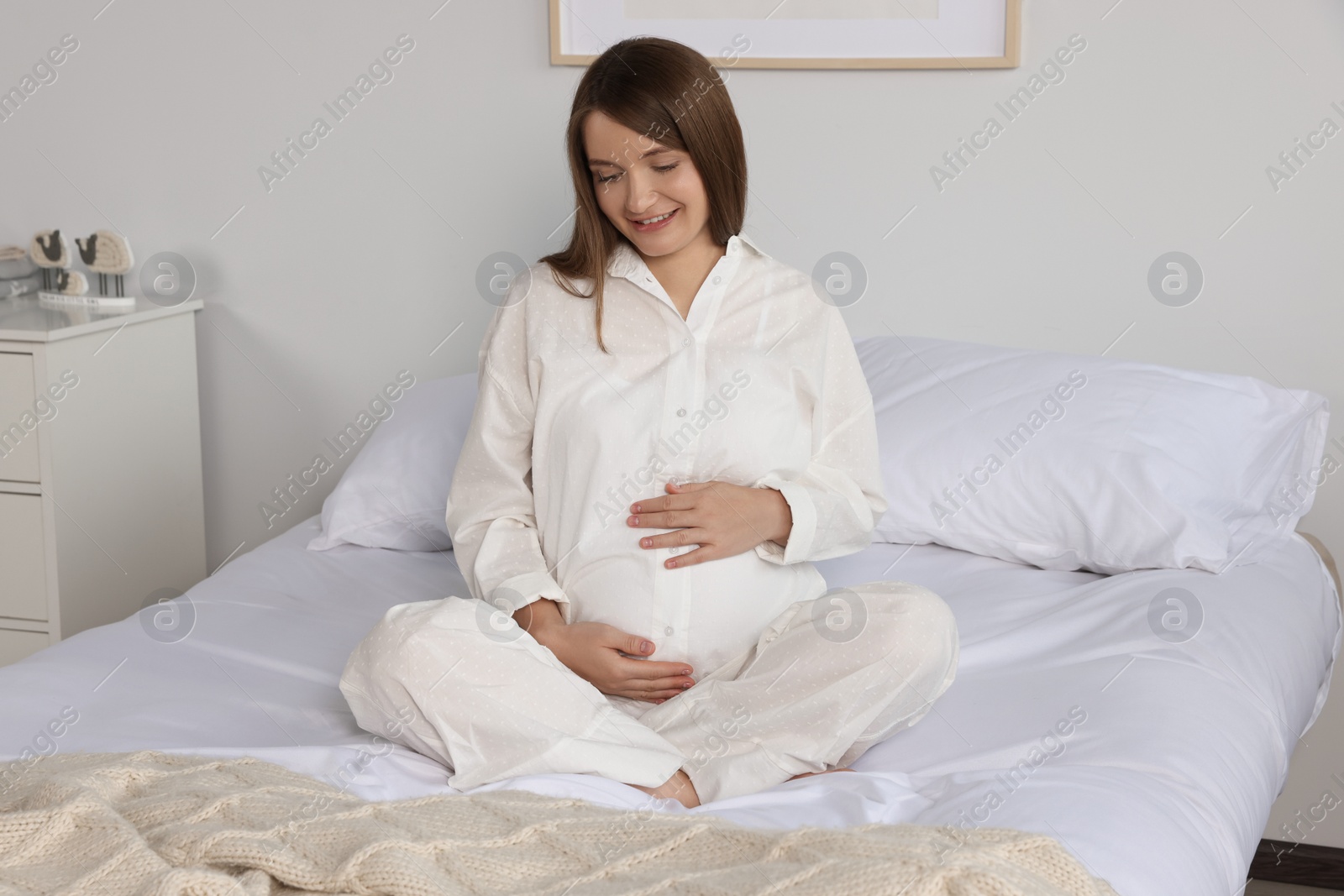 Photo of Happy young pregnant woman in pajamas on bed at home