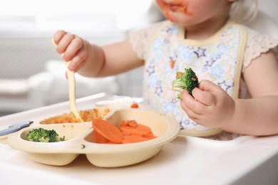 Photo of Little baby eating food in high chair, closeup