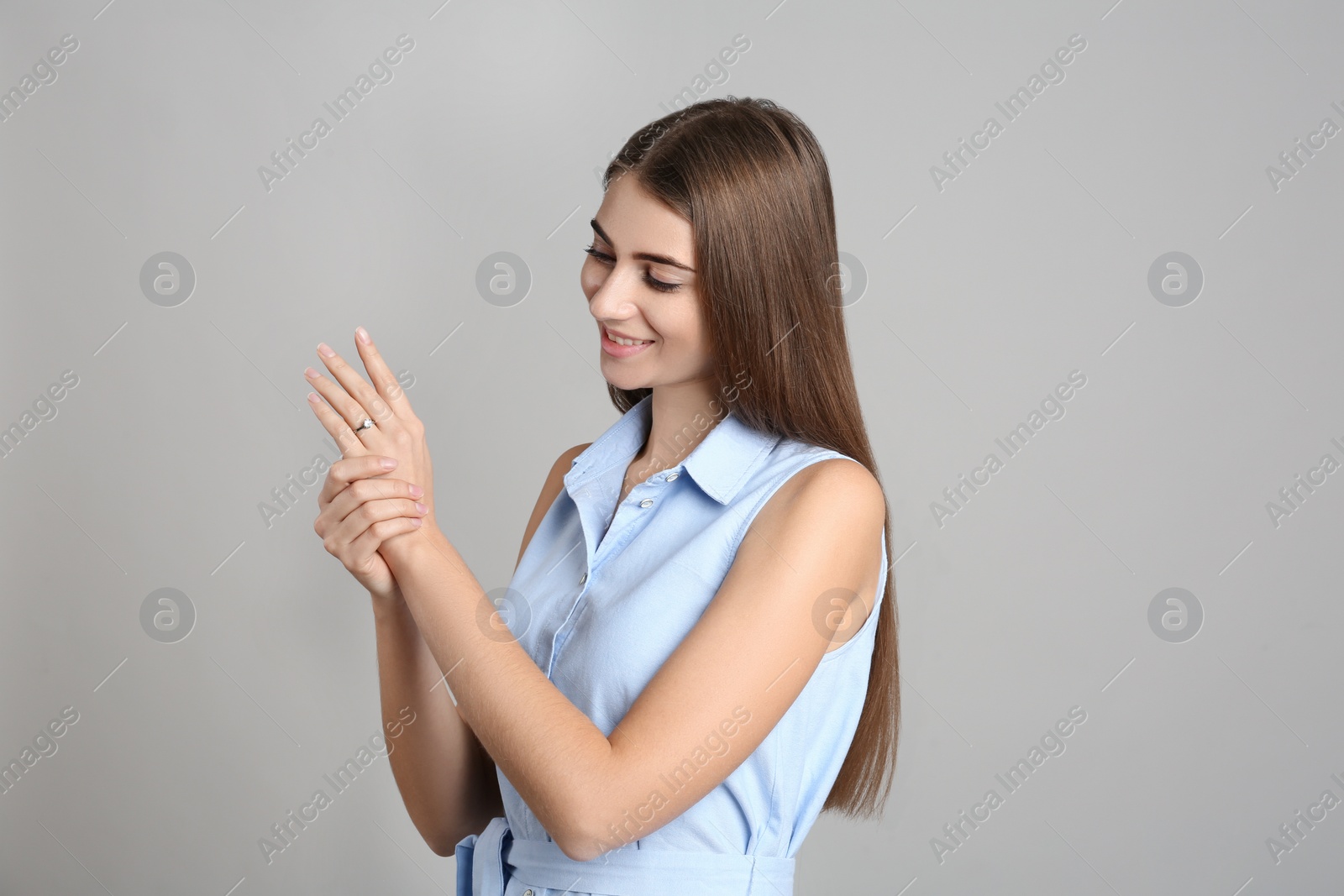 Photo of Happy young woman wearing beautiful engagement ring on grey background