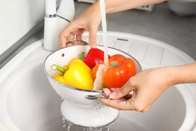 Photo of Woman washing paprika peppers in kitchen sink, closeup