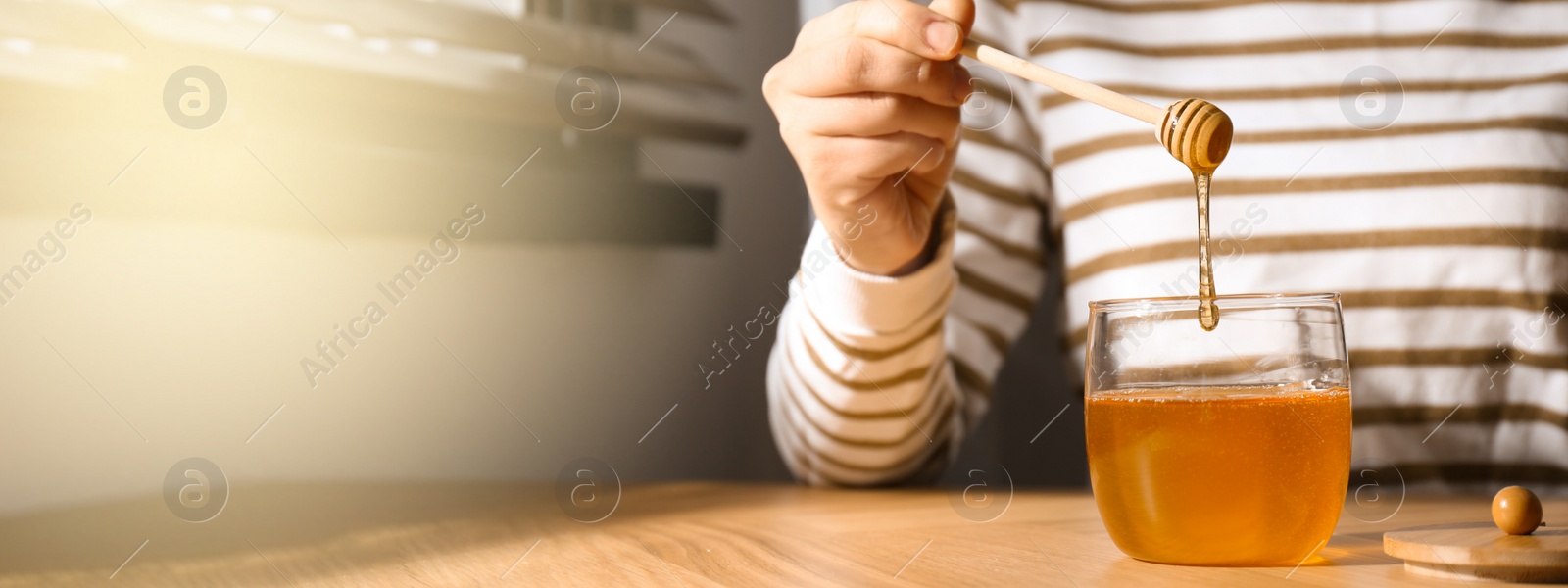 Image of Woman with honey and dipper at wooden table, closeup view with space for text. Banner design