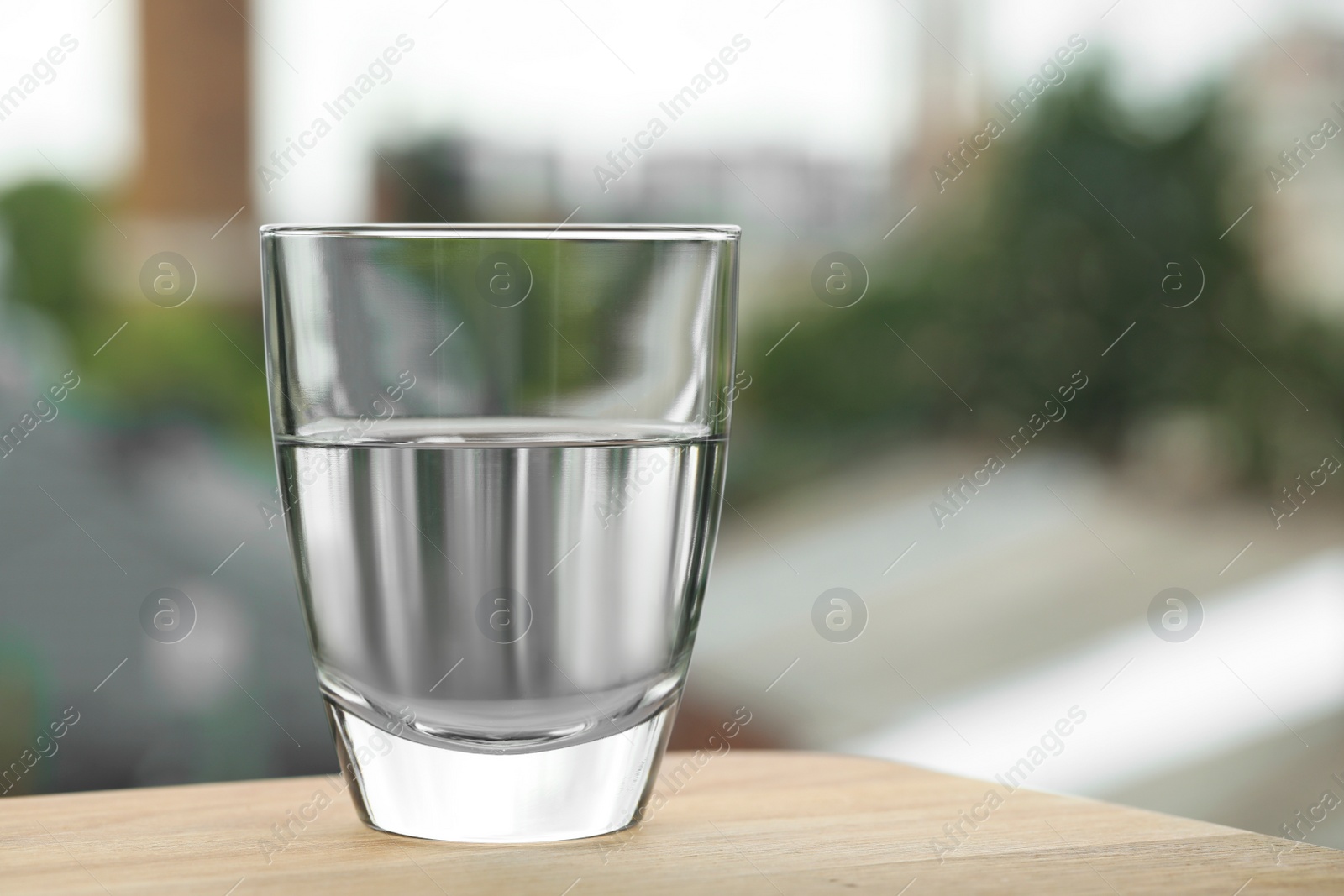 Photo of Glass of pure water on wooden table against blurred background, space for text