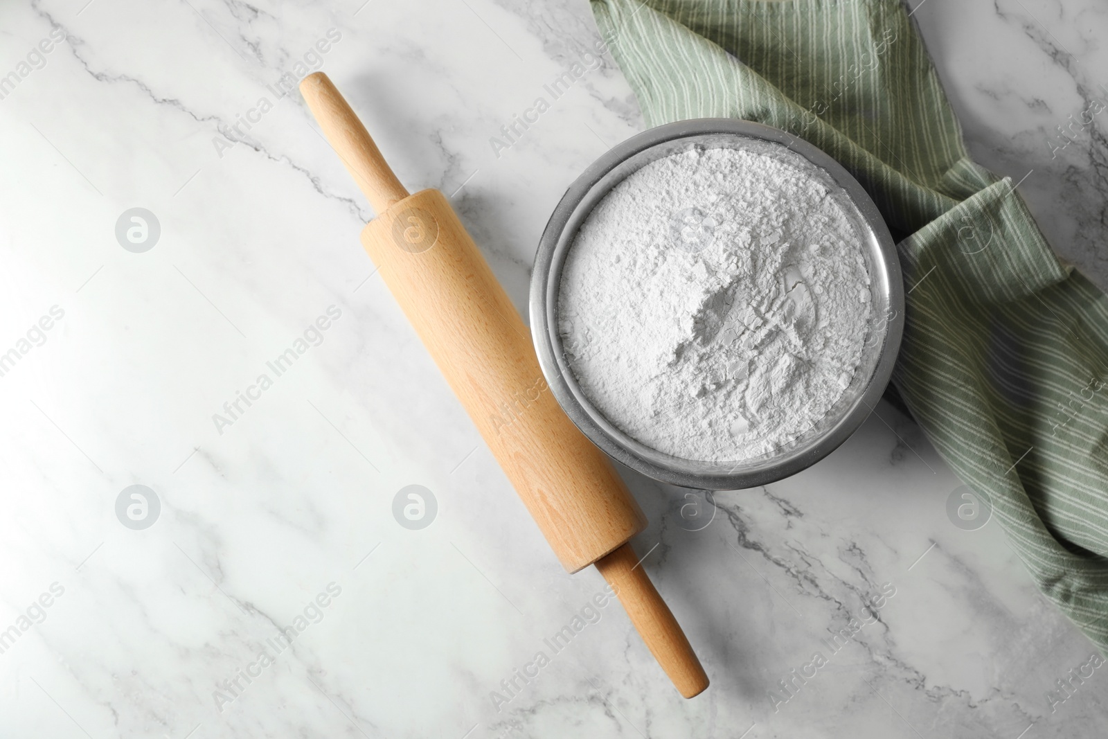 Photo of Flour in bowl, rolling pin and napkin on white marble table, top view. Space for text