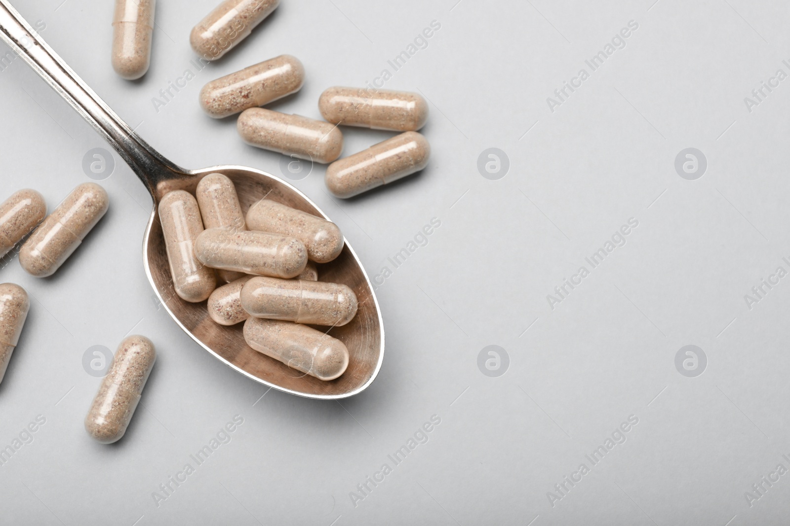 Photo of Many gelatin capsules and spoon on light grey background, flat lay. Space for text