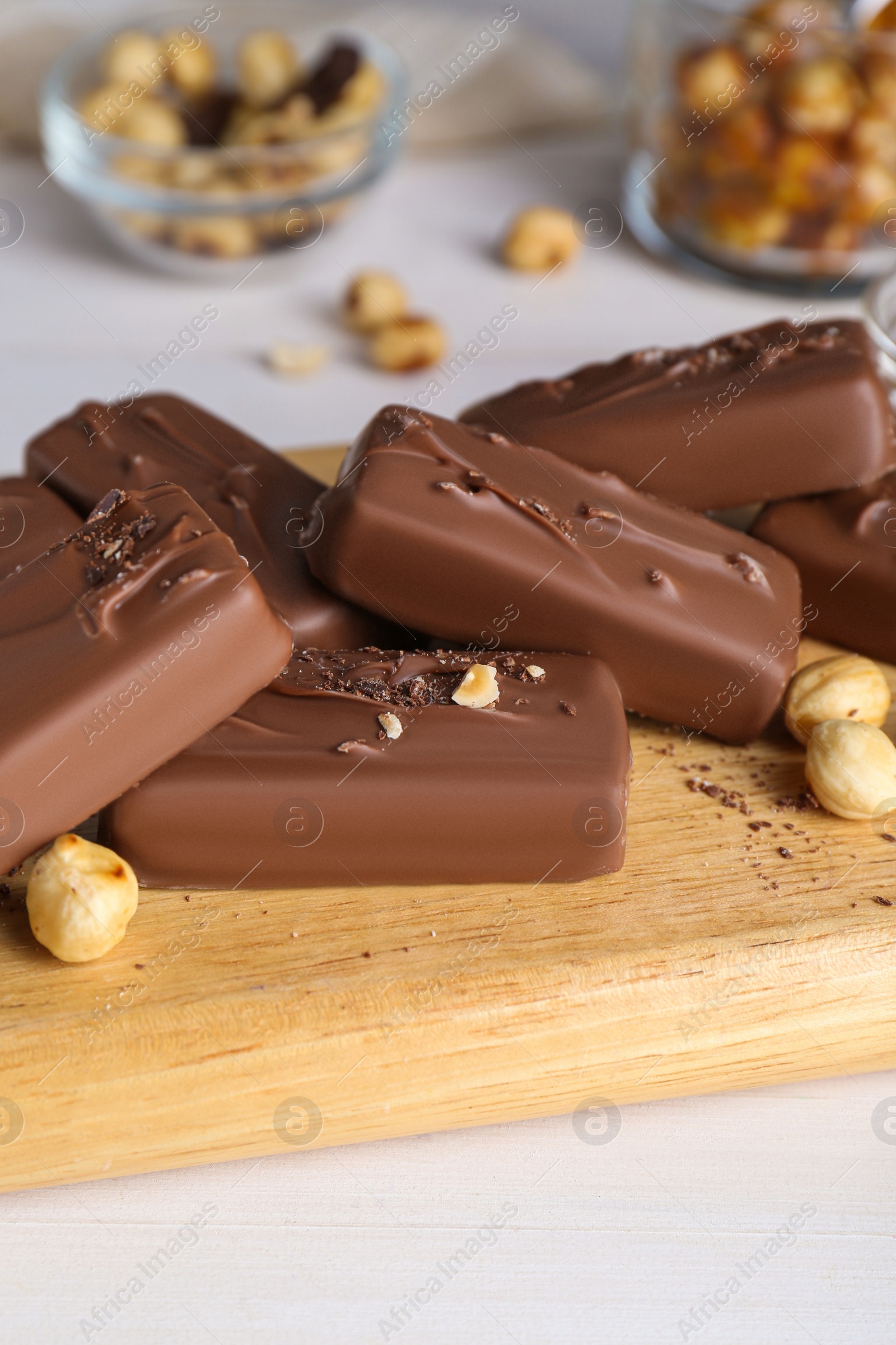 Photo of Delicious chocolate candy bars with nuts on white wooden table, closeup