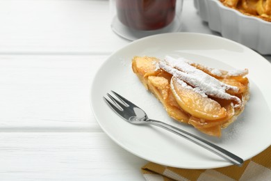 Piece of tasty homemade quince pie with powdered sugar and fork on white wooden table, space for text