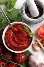 Tasty tomato paste in bowl and ingredients on table, flat lay