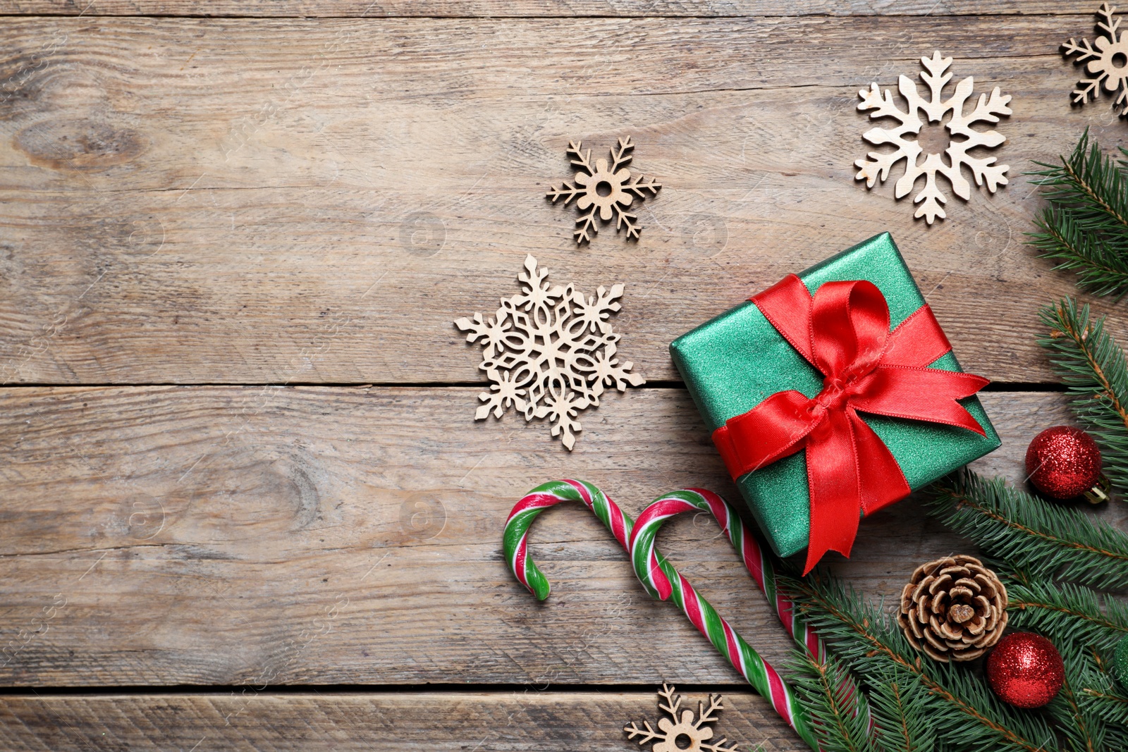 Photo of Gift box, candy canes, fir tree branches and Christmas decor on wooden table, flat lay. Space for text