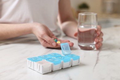 Photo of Woman with pills, organizer and glass of water at white marble table, selective focus