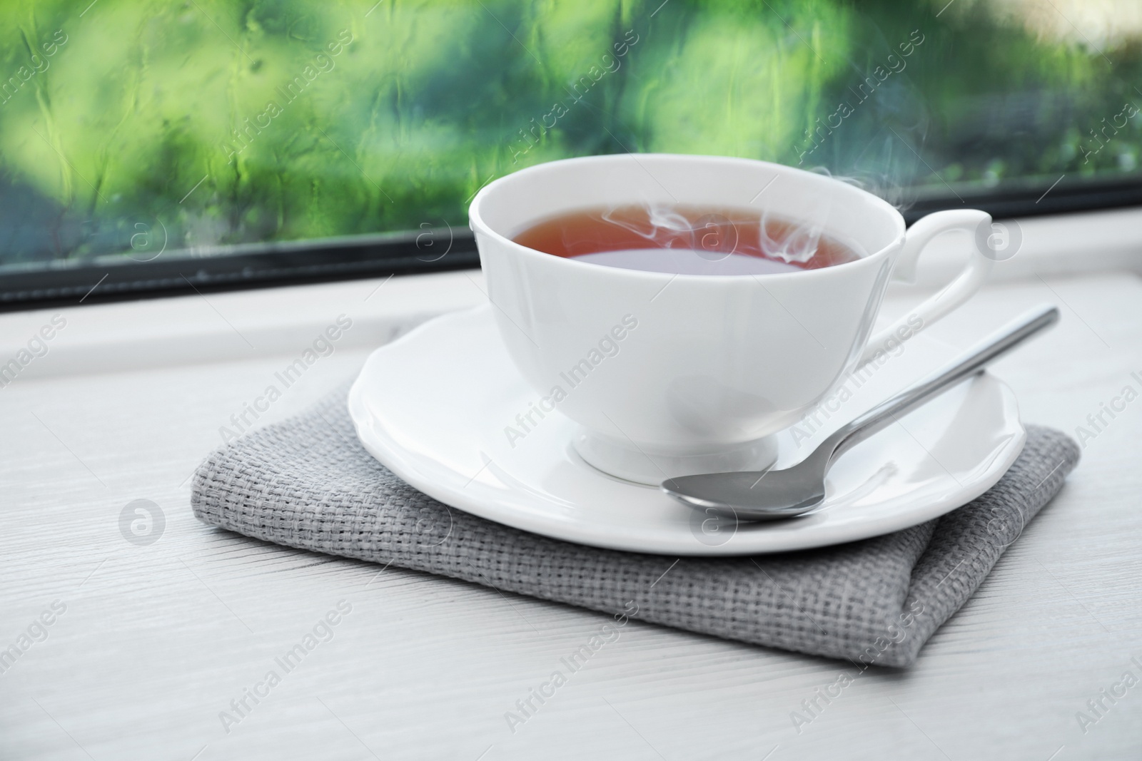 Photo of Cup of hot tea on white wooden windowsill. Rainy weather