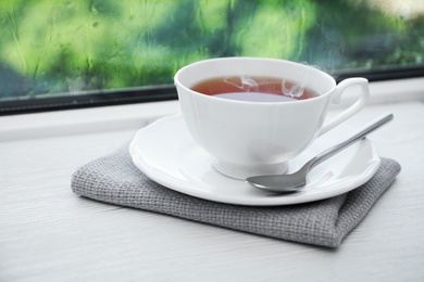 Photo of Cup of hot tea on white wooden windowsill. Rainy weather