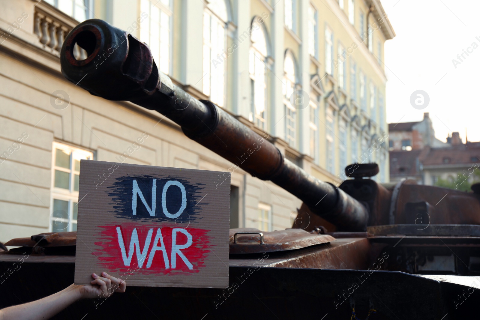 Photo of Boy holding poster with words No War near broken military tank on city street, closeup