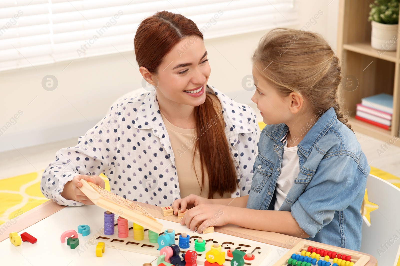 Photo of Happy mother and daughter playing with different math game kits at desk in room. Study mathematics with pleasure
