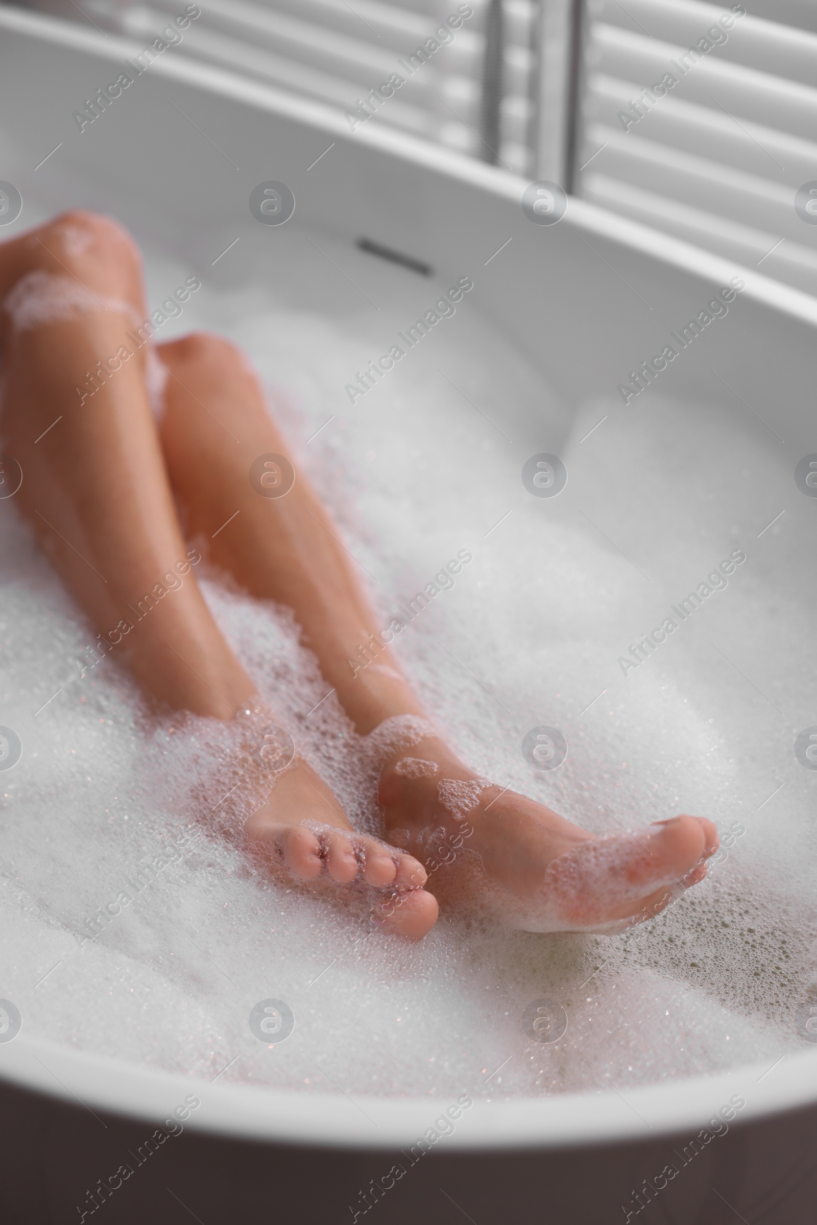 Photo of Woman taking bath in tub with foam indoors, closeup