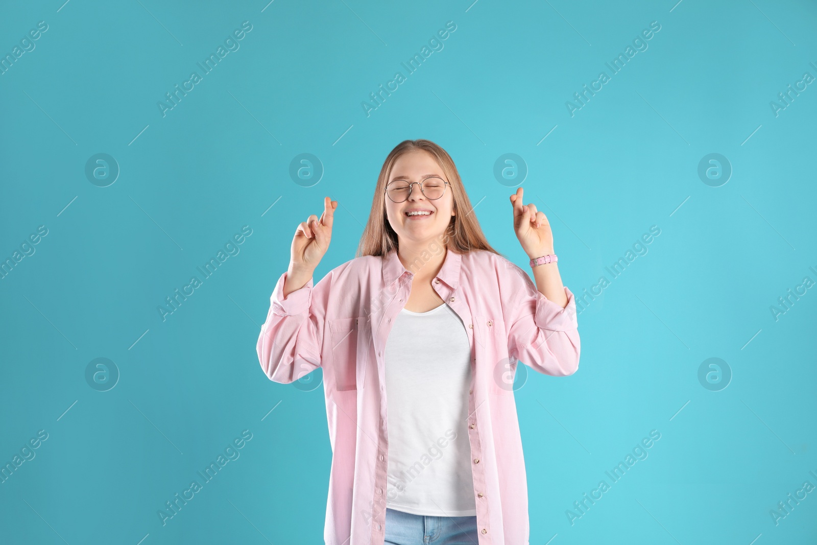 Photo of Emotional teenage girl crossing her fingers on color background