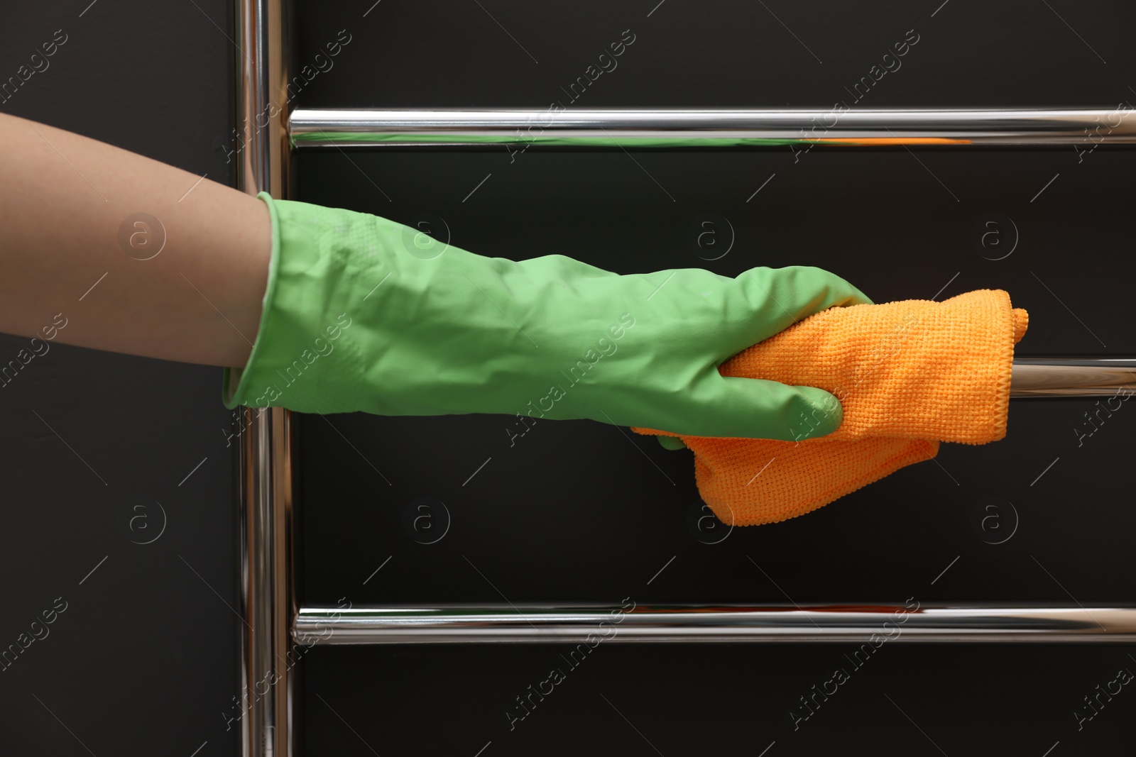 Photo of Woman cleaning heated towel rail with rag, closeup