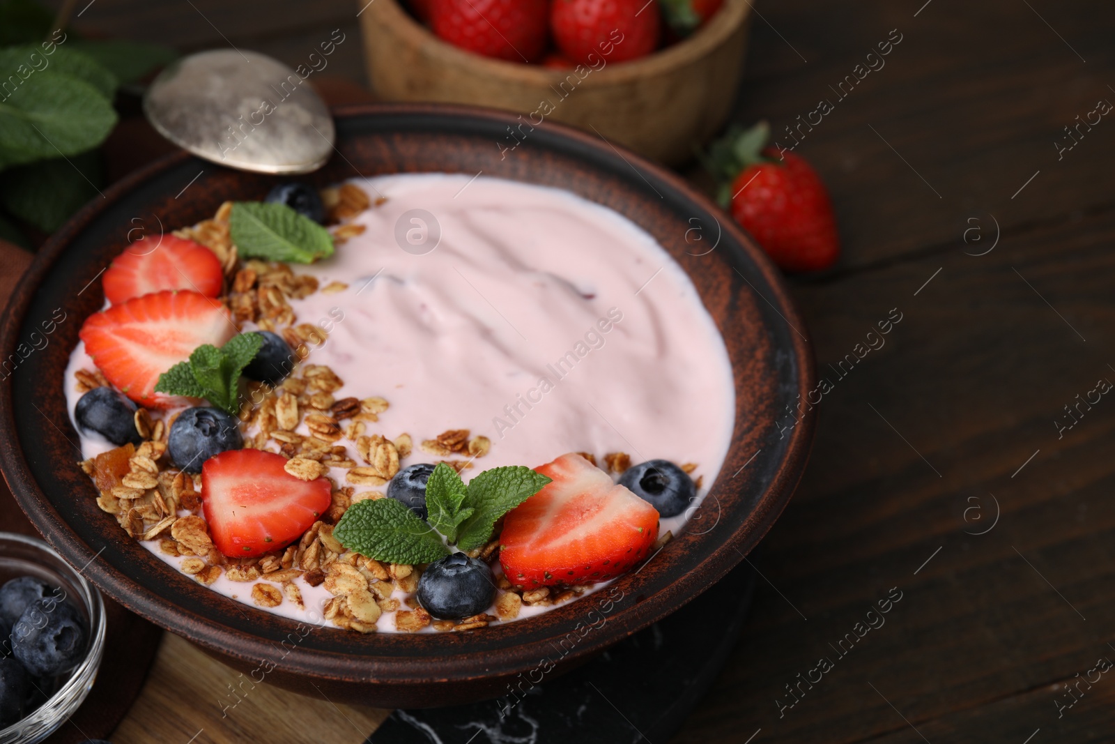 Photo of Bowl with yogurt, berries and granola on wooden table, closeup. Space for text